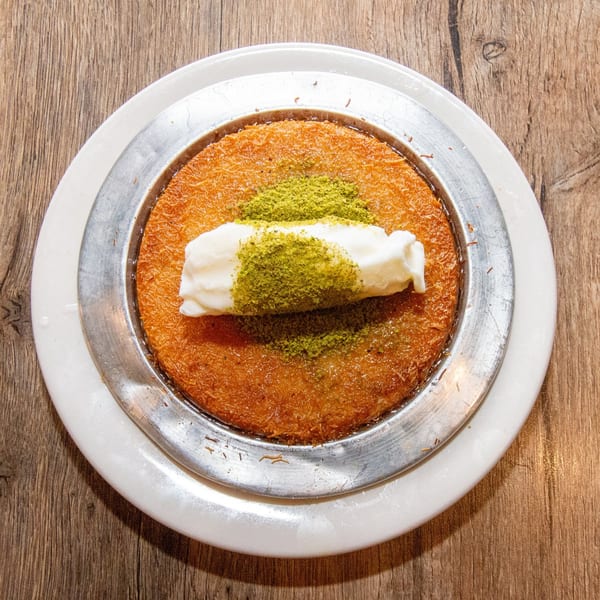 A round kunefe dessert with melted cheese, topped with clotted cream and green pistachios.