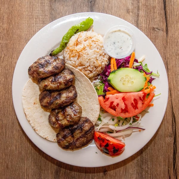 Grilled meatballs with rice, tortilla, salad, and a side of white sauce on a white plate.