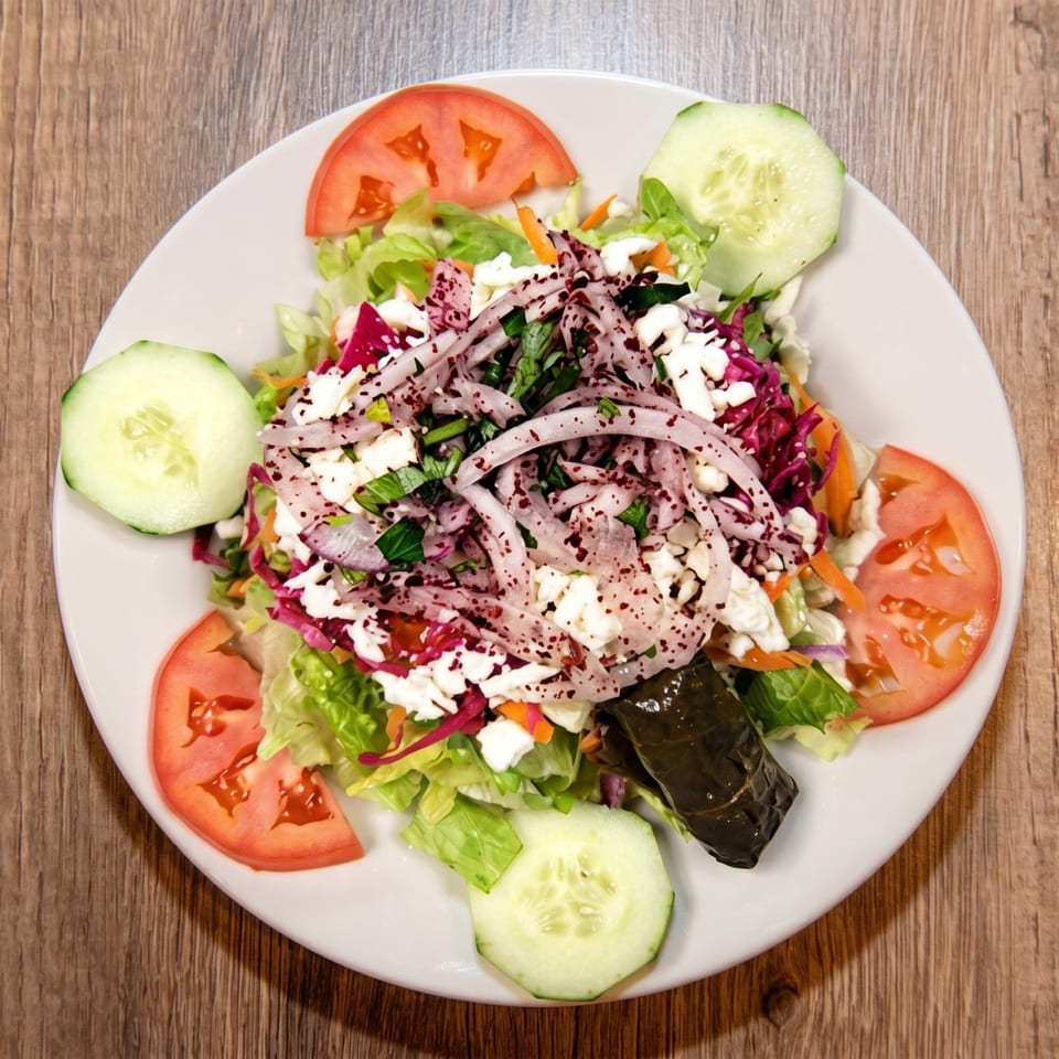 Overhead view of a fresh salad with lettuce, tomatoes, cucumbers, feta, onions, and a stuffed grape leaf.