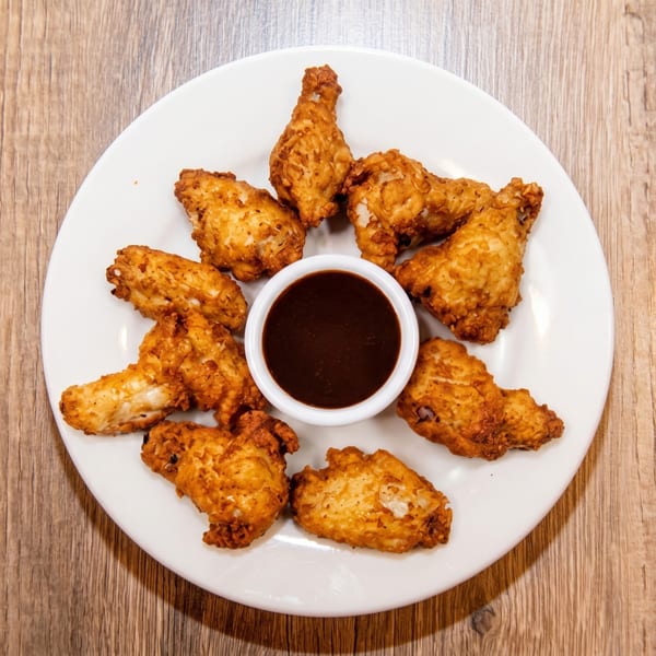 Crispy fried chicken wings arranged in a circle around a small bowl of dark dipping sauce.