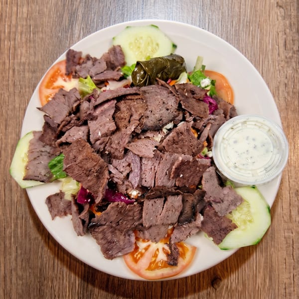 Gyro meat salad with lettuce, tomatoes, cucumbers, a stuffed grape leaf, and a side of dressing.
