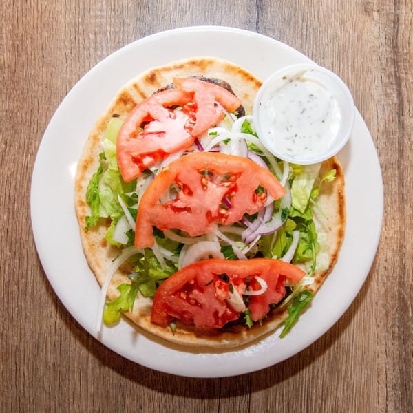 Top-down view of a gyro on pita bread with lettuce, onions, tomatoes, and a side of tzatziki.