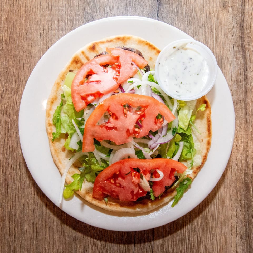 Top-down view of a gyro on pita bread with lettuce, onions, tomatoes, and a side of tzatziki.